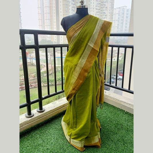 Pure Matka saree in a captivating shade of sage green, intricately woven with threads of silver and antique golden accents along its border & paired with a matching blouse piece