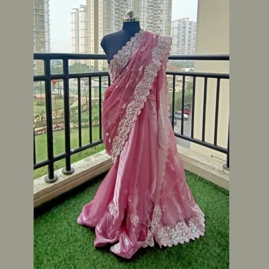 Organza saree in a delicate shade of light pink, adorned with intricate white cut work and shimmering sequence border. Paired with a matching blouse piece - Fabcentra